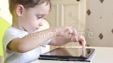 快乐的孩子坐在桌子旁，摸着触摸屏<strong>平板</strong>。 一个孩子在玩<strong>平板</strong>电脑，正在<strong>微笑</strong>。